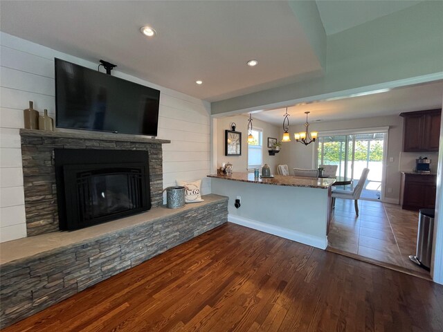 kitchen featuring dark wood-style flooring, a fireplace, recessed lighting, stone counters, and a notable chandelier