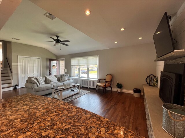 living area featuring baseboards, a fireplace with raised hearth, dark wood-type flooring, and visible vents