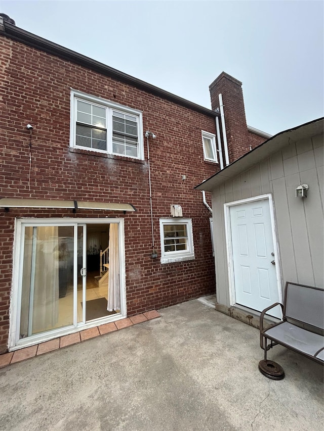 back of house with a patio area, brick siding, and a chimney