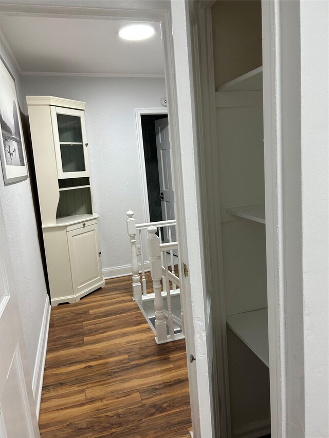 corridor with dark wood-type flooring, ornamental molding, and baseboards