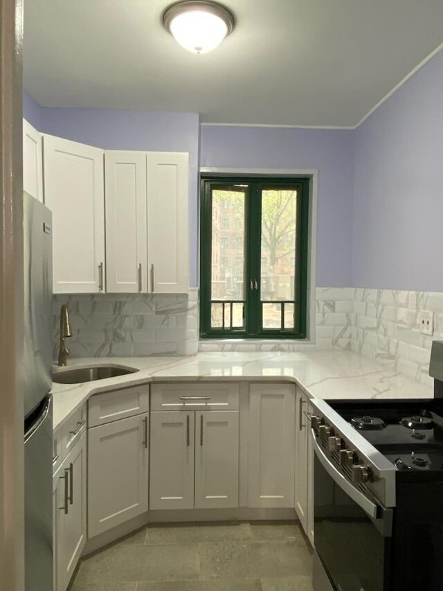 kitchen with light stone countertops, appliances with stainless steel finishes, a sink, white cabinetry, and backsplash