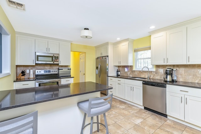 kitchen with a sink, stainless steel appliances, a kitchen breakfast bar, visible vents, and tasteful backsplash