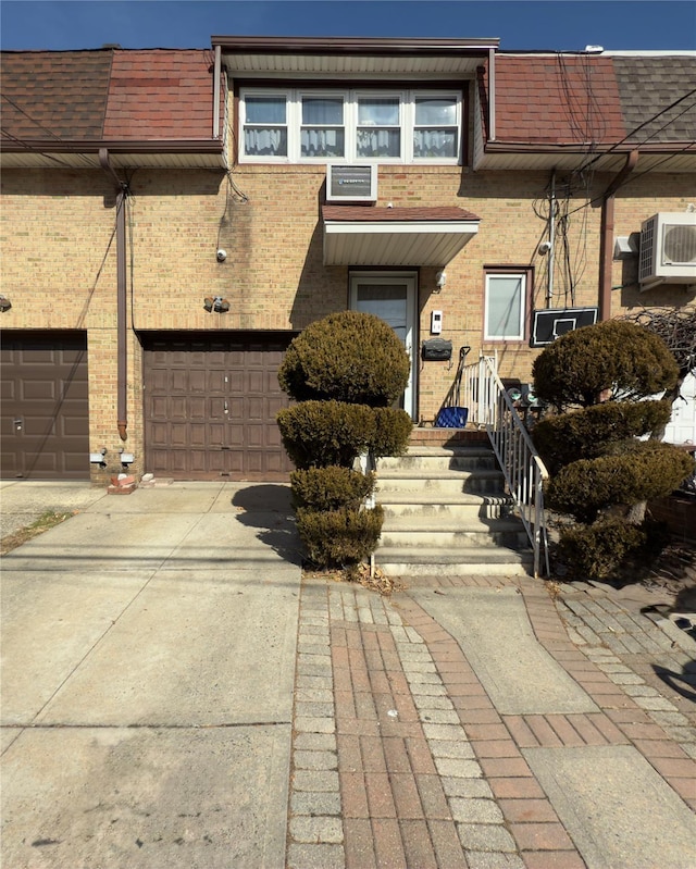 view of property featuring a garage, roof with shingles, brick siding, concrete driveway, and ac unit