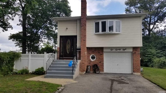 split foyer home with driveway, a chimney, brick siding, fence, and an attached garage