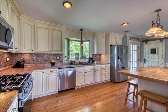 kitchen featuring a sink, light wood finished floors, stainless steel appliances, visible vents, and pendant lighting