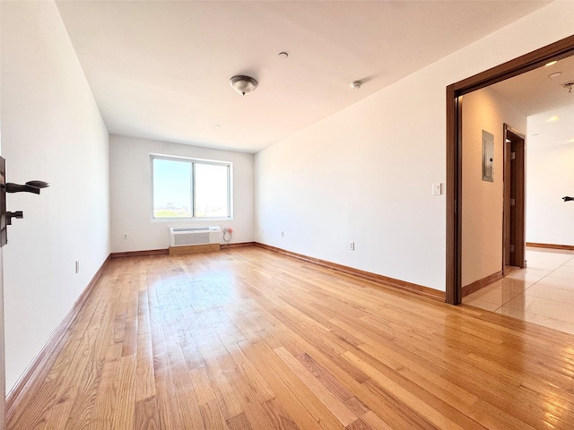 spare room featuring baseboards, a wall unit AC, and light wood-type flooring