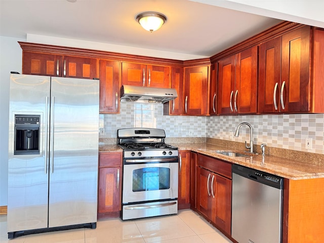 kitchen featuring backsplash, appliances with stainless steel finishes, a sink, light stone counters, and under cabinet range hood