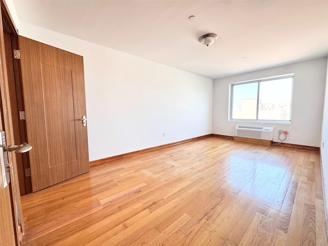 empty room with baseboards, light wood finished floors, and a wall mounted air conditioner