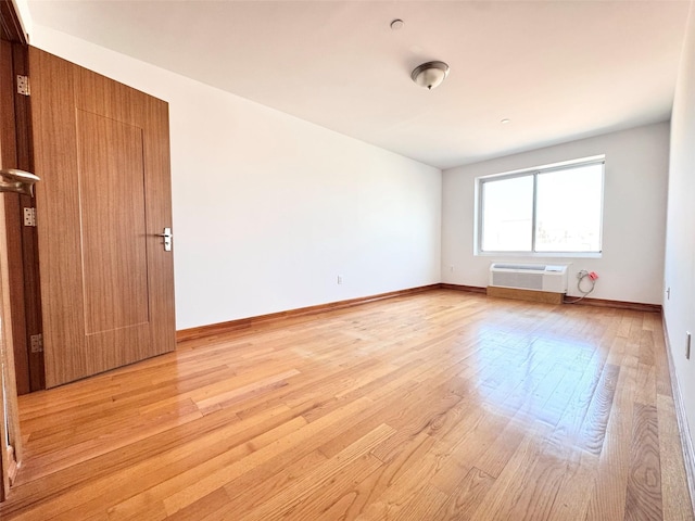 spare room featuring baseboards, an AC wall unit, and light wood-style flooring