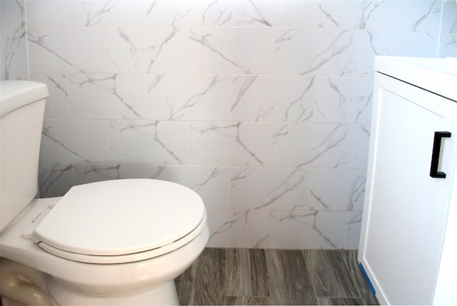 half bath featuring tile walls, vanity, toilet, and wood finished floors