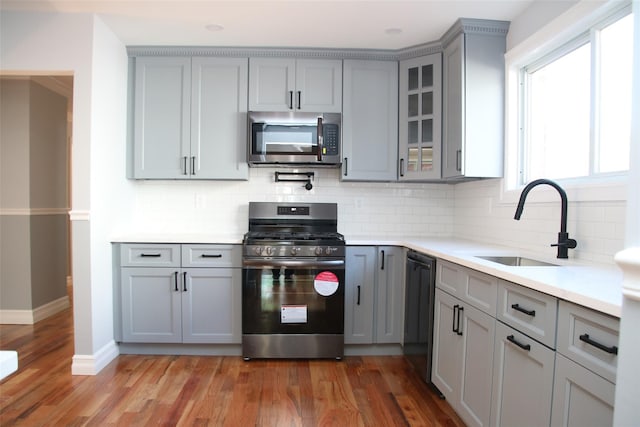 kitchen featuring glass insert cabinets, light wood-type flooring, gray cabinets, a sink, and stainless steel appliances