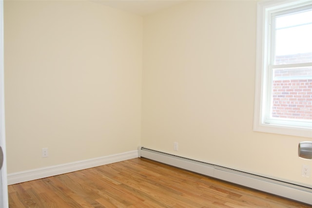empty room with light wood-type flooring, a baseboard radiator, and baseboards