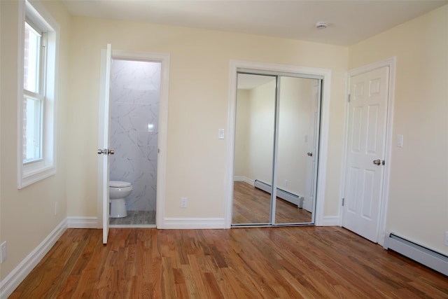 unfurnished bedroom with wood finished floors, ensuite bath, a baseboard heating unit, and a closet