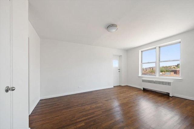 empty room featuring radiator, wood finished floors, and baseboards