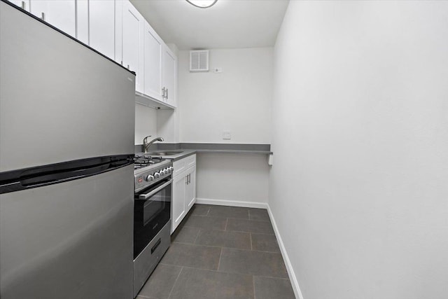 kitchen with appliances with stainless steel finishes, a sink, white cabinetry, baseboards, and dark tile patterned floors