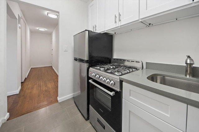 kitchen with range with gas cooktop, white cabinetry, a sink, baseboards, and freestanding refrigerator