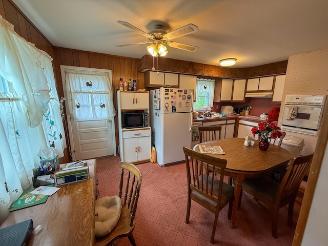 dining area featuring a ceiling fan, wood walls, and light colored carpet