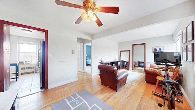 living area featuring baseboards, ceiling fan, radiator heating unit, and light wood-type flooring