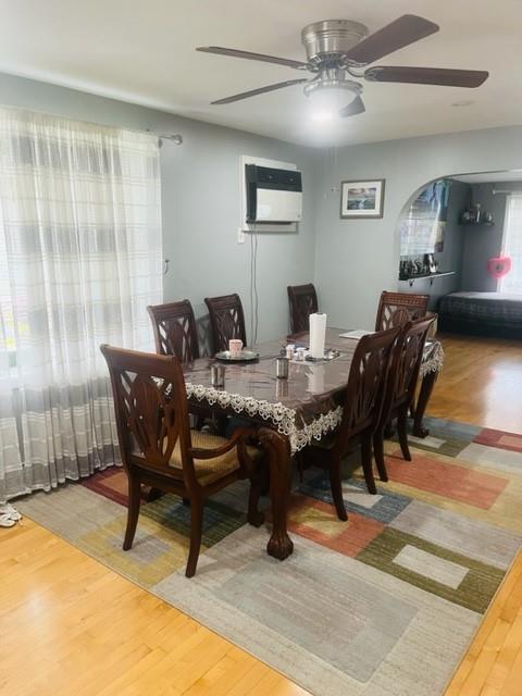 dining space featuring a wall unit AC, arched walkways, a ceiling fan, and wood finished floors