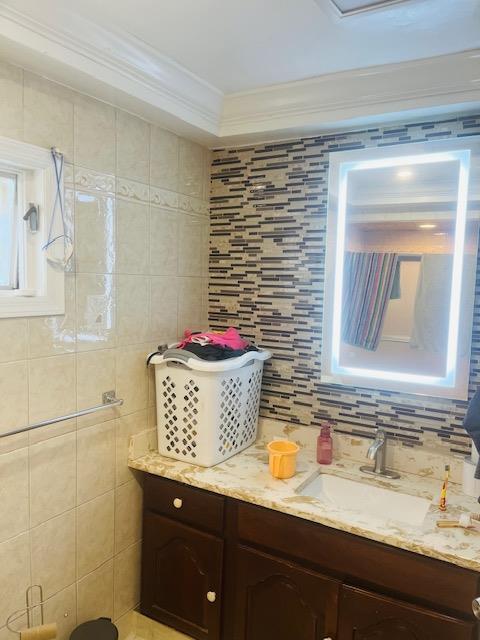 bathroom with tile walls, vanity, crown molding, and decorative backsplash