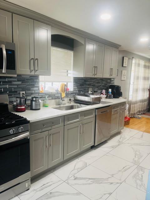 kitchen featuring marble finish floor, backsplash, light countertops, appliances with stainless steel finishes, and gray cabinets