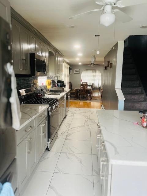 kitchen with marble finish floor, a ceiling fan, backsplash, appliances with stainless steel finishes, and light stone counters
