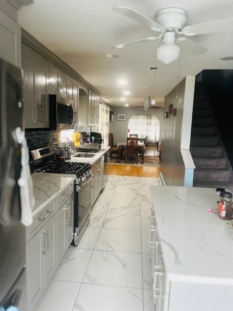 kitchen with a ceiling fan, a sink, stainless steel appliances, light stone countertops, and marble finish floor