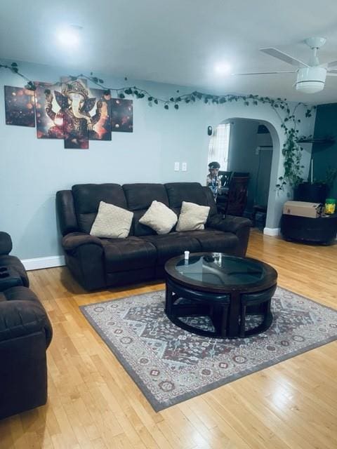 living room featuring arched walkways, a ceiling fan, baseboards, and wood finished floors