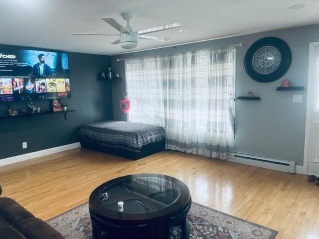 bedroom featuring multiple windows, wood finished floors, a ceiling fan, and a baseboard heating unit