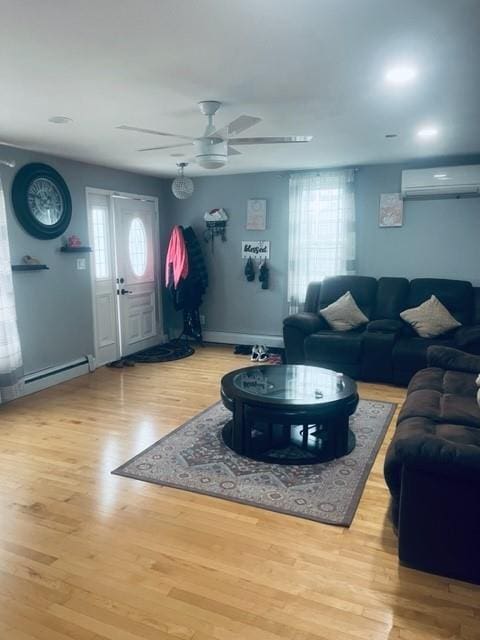 living area featuring baseboards, wood finished floors, a ceiling fan, and an AC wall unit