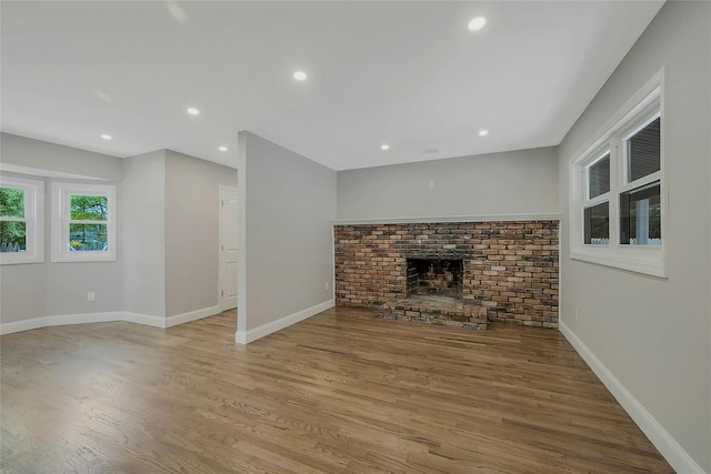 unfurnished living room with a brick fireplace, recessed lighting, baseboards, and wood finished floors
