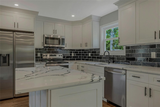 kitchen featuring a kitchen island, light stone countertops, a sink, white cabinets, and stainless steel appliances