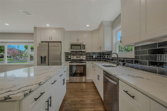 kitchen featuring dark wood-style flooring, appliances with stainless steel finishes, light stone counters, a sink, and white cabinetry