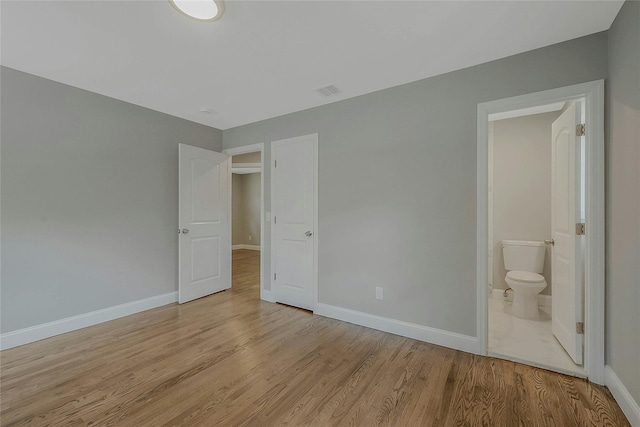 unfurnished bedroom with baseboards, visible vents, light wood finished floors, and ensuite bath