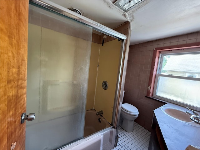 bathroom with shower / bath combination with glass door, tile patterned flooring, vanity, toilet, and tile walls