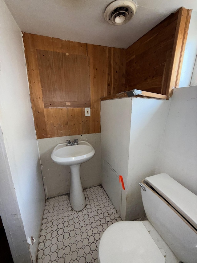 half bathroom with wood walls, toilet, and visible vents