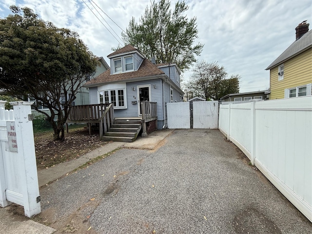 view of property exterior with fence, a gate, a wooden deck, and roof with shingles