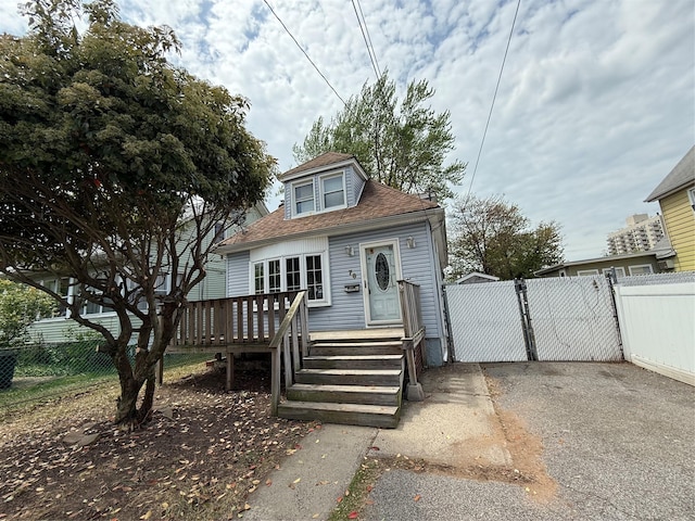 bungalow-style home with fence, a wooden deck, and roof with shingles