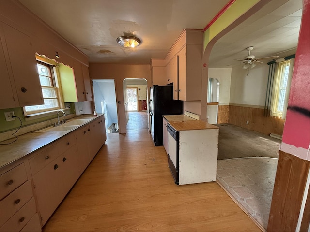 kitchen featuring arched walkways, a ceiling fan, a sink, and a wainscoted wall