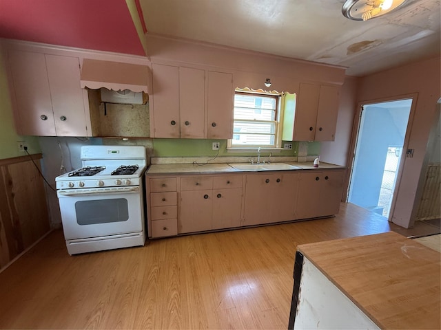 kitchen with a sink, light countertops, white gas range oven, light wood finished floors, and custom range hood