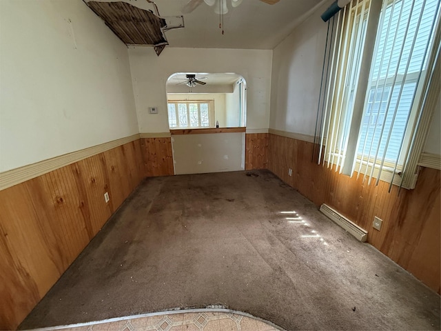 unfurnished room with wood walls, a ceiling fan, and a wainscoted wall