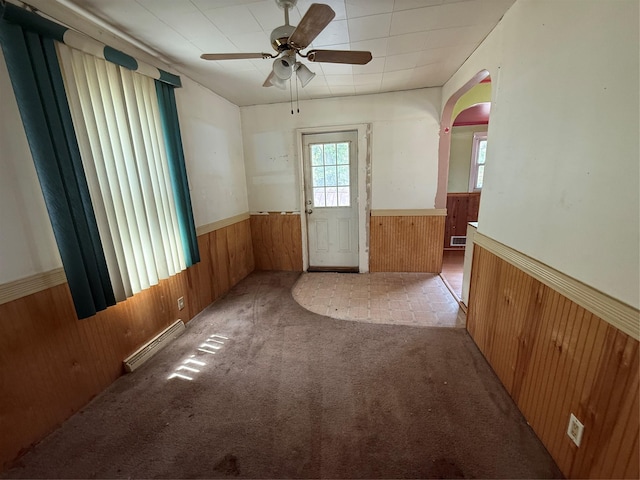 carpeted empty room featuring visible vents, wood walls, wainscoting, ceiling fan, and arched walkways