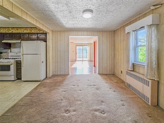 1994 Pine St, North Baldwin, NY 11510 - kitchen with white appliances, radiator, under cabinet range hood, dark brown cabinetry, and wood walls