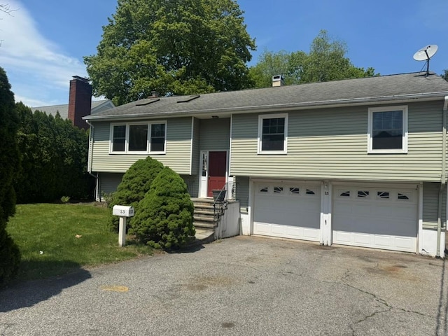 bi-level home featuring an attached garage, a chimney, entry steps, and aphalt driveway