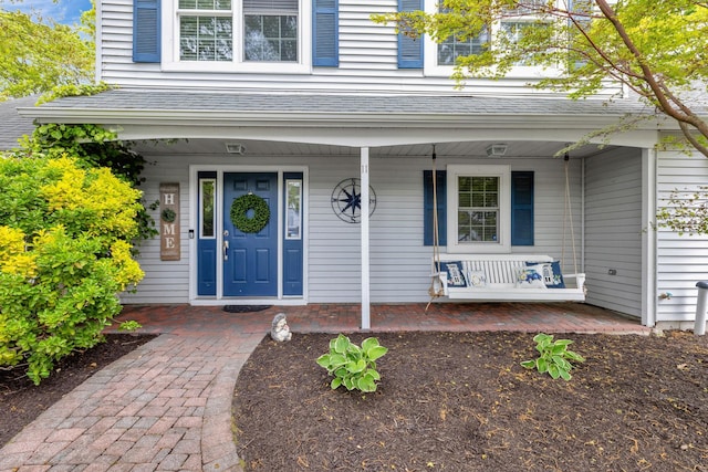 view of exterior entry featuring a porch and a shingled roof
