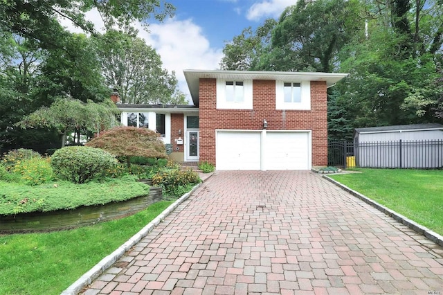 split level home with a front yard, a garage, brick siding, decorative driveway, and fence