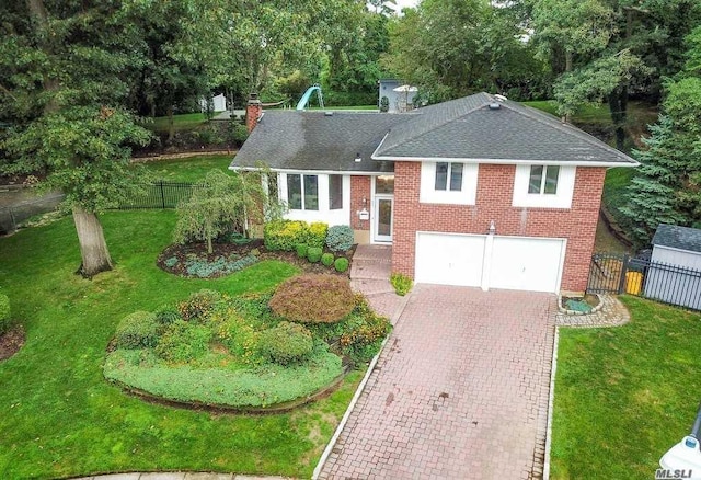 tri-level home with brick siding, a shingled roof, a front lawn, and fence