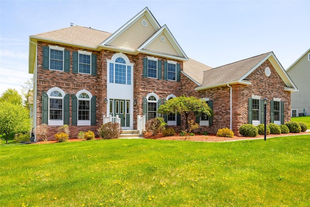 view of front of house featuring brick siding, a front yard, and roof with shingles