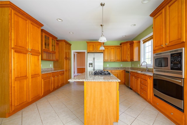 kitchen featuring brown cabinetry, a kitchen island, light stone countertops, a sink, and stainless steel appliances