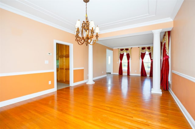 empty room featuring crown molding, ornate columns, a notable chandelier, and light wood-style floors